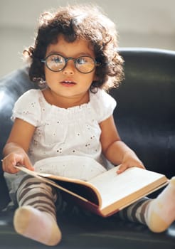 Relax, sofa and a child reading a book for education, learning and knowledge in a house. Morning, smart and a girl, kid or baby with a story and glasses for studying or childhood on the couch.