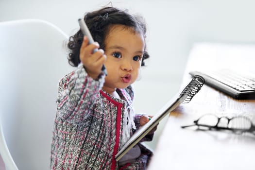 Thinking, playing and a child with a notebook for drawing, art and creativity for a home hobby. Idea, inspiration and a girl, kid or baby with paper for education, learning and a picture at a desk.