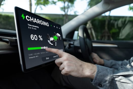 Electric car driver checks battery charging status, range and charging limit on app screen in the car. Smart technology device show EV car recharging data of electric storage in car battery innards.