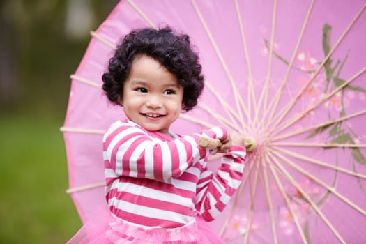 Umbrella, happy and girl child in a garden walking on the grass on summer weekend. Adorable, playful and young kid, baby or toddler with curly hair playing on the lawn in outdoor field or park