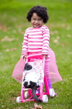 Portrait, happy kid and kitten for playing with baby carriage on grass, garden or backyard of family home. Little girl, pet and pushing of stroller together for fun, imagine or game for bond by care.
