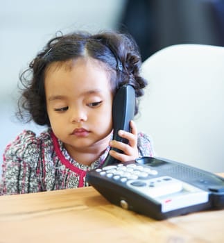 Listening, talking and a child on a telephone phone call for communication in a house. Home, contact and a girl, kid or baby speaking on a landline for conversation, play or a discussion at a desk.
