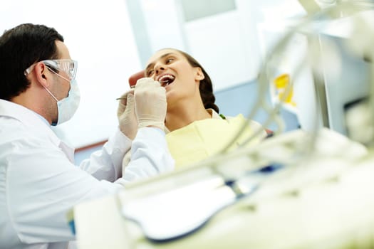 Young woman sitting in dentists chair while doctor examining her teeth