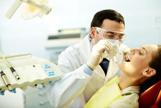 Young woman sitting in dentists chair while doctor examining her teeth