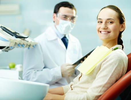 Smiling woman sitting in dentists chair with doctor on background