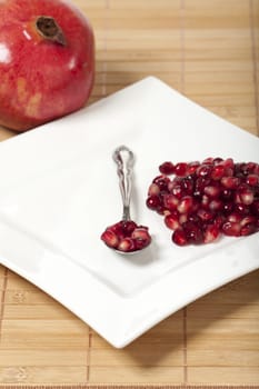 Pomegranate and a white plate with pomegranate seeds on a spoon