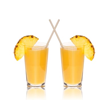 Two glasses of pineapple juice with drinking straw and a piece of pineapple fruit mirrored on the edge of the glass at the bottom isolated against white background