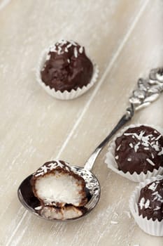 Dark chocolate coated coconut rice pudding truffle and a silver spoon with a halved truffle on a wooden tray
