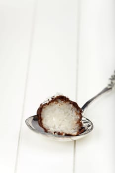 Dark chocolate coated half coconut rice pudding truffle on a silver spoon