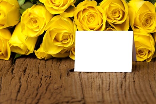 Bouquet of yellow roses and a writable white card on an old wooden board