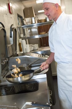 Male cook making chicken in frying pan in kitchen