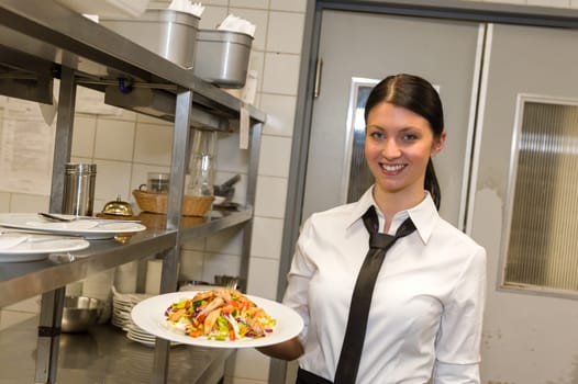 Smiling waitress serving salad on plate in restaurant's kitchen
