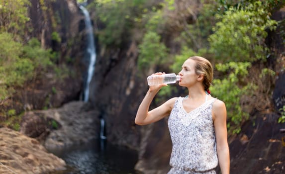 girl drinks water from a bottle on the background of a waterfall.