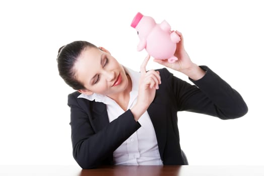 Happy business woman with her savings in piggy bank at the desk, isolated