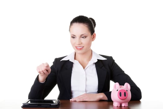 Businesswoman at the desk with tablet and piggy bank, isolated on white. Modern banking concept.