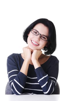 Pretty, happy, young woman in casual clothes sitting at the desk, isolated on white