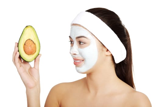 Young woman holding avocado heaving face clay mask on the face in a spa