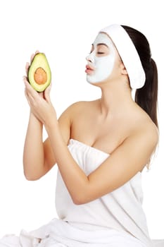 Young woman holding avocado heaving face clay mask on the face in a spa