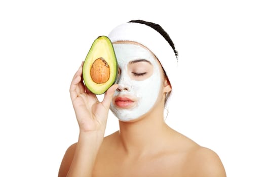 Young woman holding avocado heaving face clay mask on the face in a spa