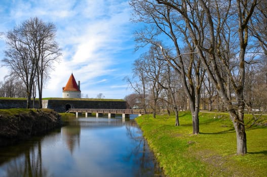 Kuressaare castle tower with blue sky in background and water with reflections in foreground (Saarema, Estonia)