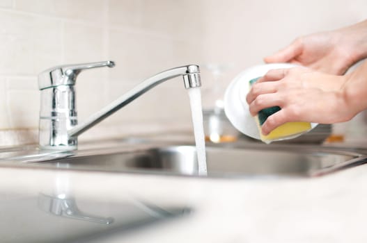 woman hand holding yellow sponge and washing saucer with washed dishes in background