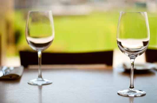 two empty glass goblets on wooden table in restaurant (extremely shallow depth of field, focus on front goblet)