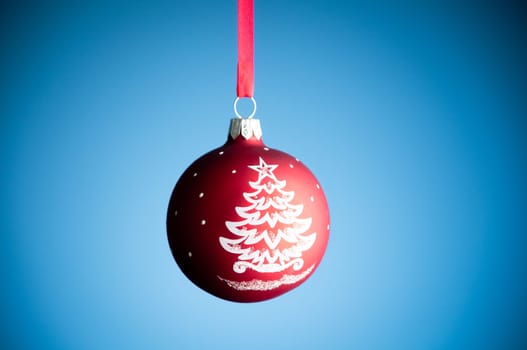 red christmas toy ball hanging on the red ribbon against blue background
