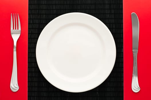 empty white plate on black table with knife and fork on red napkin by the sides of the plate