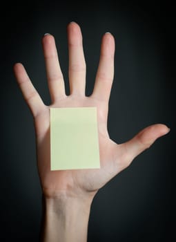 female hand with sticky office note on dark background . Note is blank and yellow