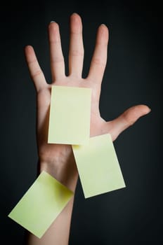 female hand with three office sticky notes on dark background . All notes are blank and yellow