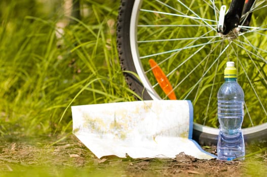 blue bottle of water and map on the ground in the forest near the bicycle wheel