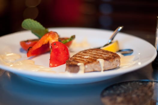 tasty steak and vegetables on white plate at restaurant with colorful background (extremely shallow depth of field)