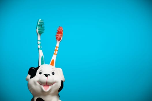 two toothbrushes in the glass resembling smiling dalmatian dog's head against blue background