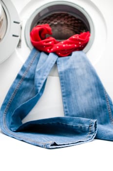 Blue jeans and red shirt hanging out from the door of the washing machine. Space for copy on the floor. Focus is on the lower part of the jeans. Isolated on white background.