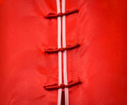 Close-up view of traditional clothing in Vietnam. Detail of woman vietnamese dress. Bright red satin or silk fabric with white lines and three fasteners in centre. Traditional clothes and costumes.