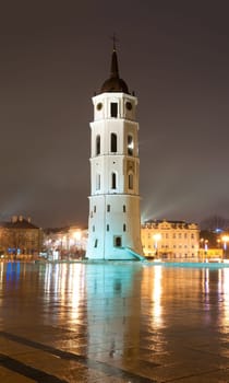 Vilnius cathedral bell tower at rainy night with reflection. Lithuania, Europe. Famous landmark. Place for copy in foreground and dark night sky in background.