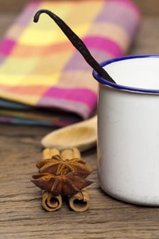 Cinnamon sticks,anise stars and a vanilla bean in an enamel cup on a rustic wooden plate