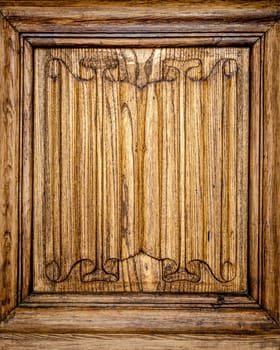 Part of door adorned by vintage ornate patterns. Front view of wooden door fragment with stylish symmetrical carvings on it.
