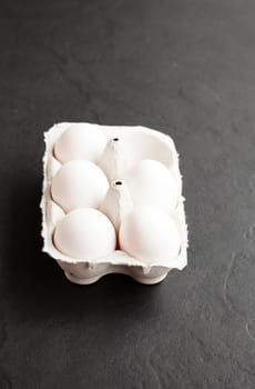 Chicken eggs in white carton on dark background