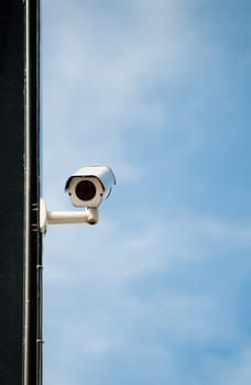 modern security camera on wall of building in street of city with blue sky in background