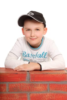 A boy sits behind a stone wall,seems to be waiting and looks kindly into the camera.