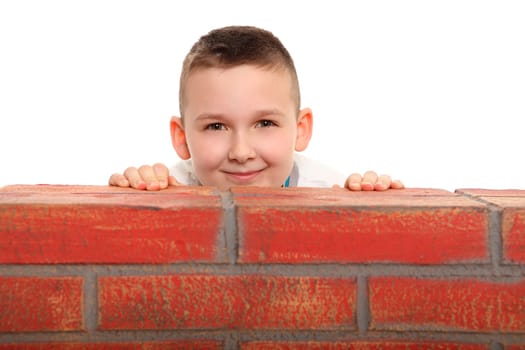 A boy sits behind a stone wall and seems to want to hide. He looks cunningly out from behind the wall