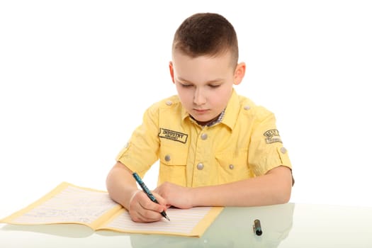 A young student sits at a desk and writes intently in his notebook.