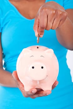 Black african american woman inseerting coin inside a smiling Piggy bank isolated on white background - African people