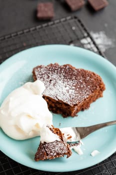 Closeup of slice of chocolate cake and whipped cream on plate resting on mesh metal tray with chocolate squares in background