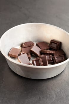 Closeup of bowl containing pieces of chocolate on dark background