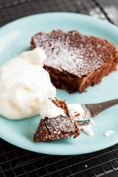 Closeup of slice of chocolate cake and whipped cream on plate resting on mesh metal tray
