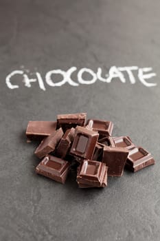 Closeup of pile of chocolate squares with word chocolate written in chalk on dark background