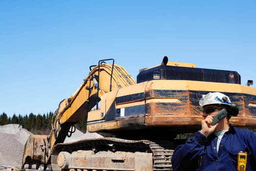 engineer, mechanic talking in phone with large bulldozer inside construction site