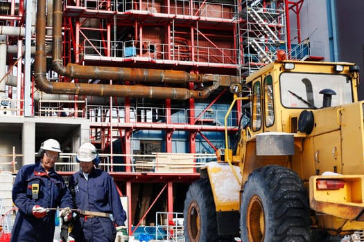 two site workers in hard-hats inside large construction industrial site.